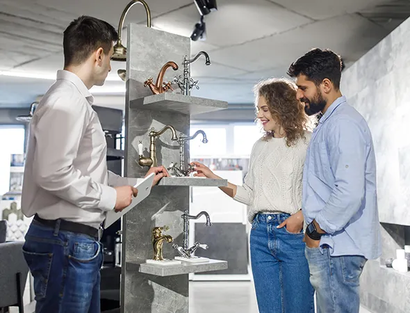 Three individuals assess a bathroom sink during a renovation project, discussing design and functionality options.